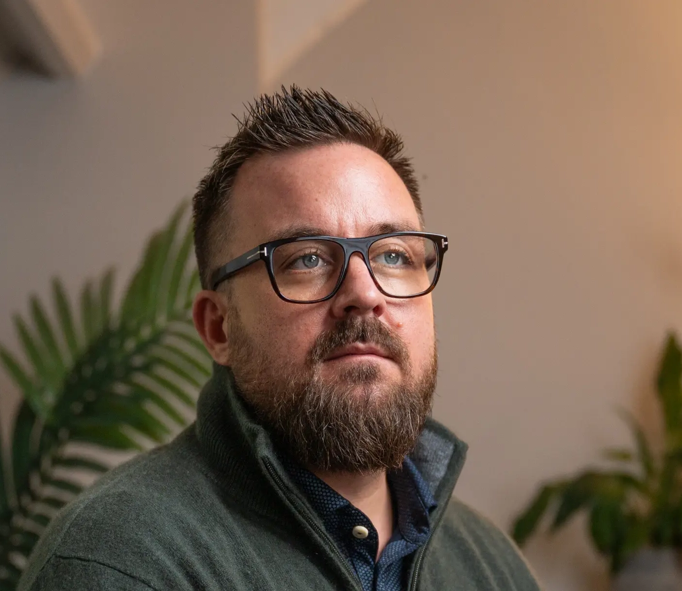 Julian Hamlin wearing glasses in a moody close-up portrait, psychologist and psychotherapist, with a plant in the background